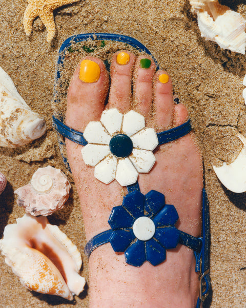 Close up of a foot with painted nails wearing a blue floral sandal in the sand.